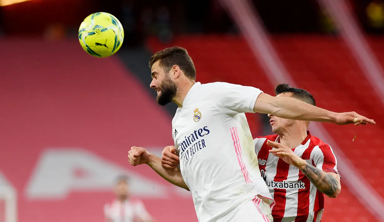 Pemain Real Madrid, Nacho Fernandez, duel udara dengan pemain Athletic Bilbao, Alex Berenguer, pada laga Liga Spanyol di Stadion San Mames, Minggu (16/5/2021). Real Madrid menang dengan skor 1-0. (AFP/Ander Gillenea)