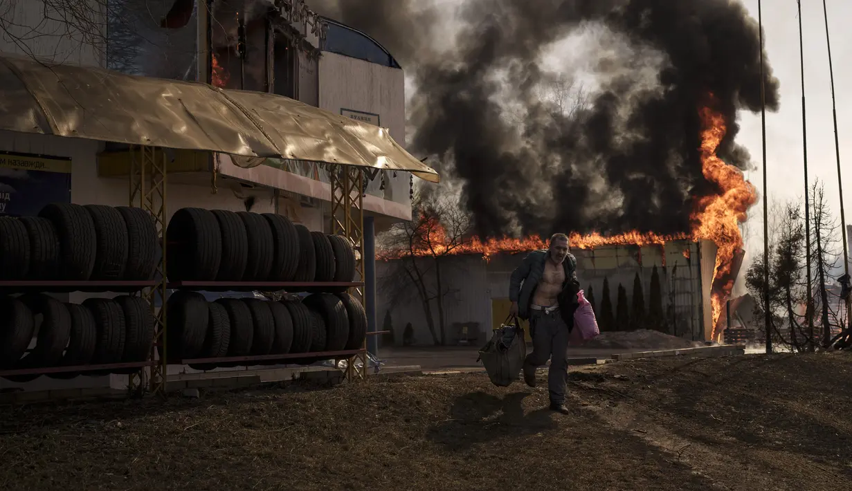 Seorang pria mengambil barang-barang dari toko yang terbakar setelah serangan Rusia di Kharkiv, Ukraina, 25 Maret 2022. (AP Photo/Felipe Dana)