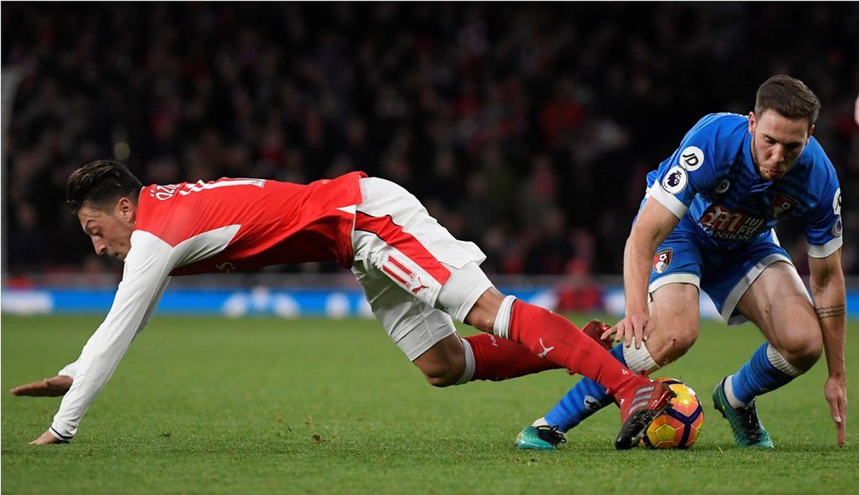 Pemain Arsenal, Mesut Ozil, terjatuh saat berebut bola dengan pemain AFC Bournemouth, Dan Gosling, dalam laga pekan ke-13 Premier League 2016-2017 di Stadion Emirates, Minggu (27/11/2016). (Reuters/Toby Melville)