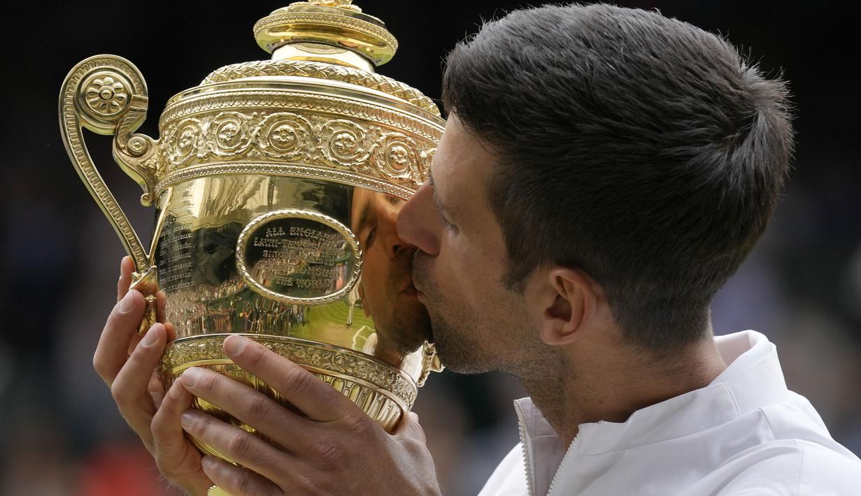 Petenis Serbia, Novak Djokovic cium Piala Wimbledon usai kalahkan petenis Italia, Matteo Berrettini di partai puncak tunggal putra. Kemenangan ini mengantarkan Djokovic menyamai rekor Nadal dan Federer sebagai petenis yang mampu mendapatkan 20 gelar Grand Slam. (Foto: AP/Kirsty Wigglesworth)