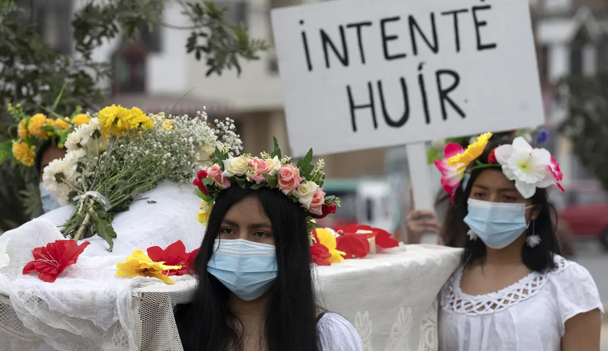 Rombongan teater Vichama melakukan prosesi kamar mayat berjudul "Kami Ingin Diri Sendiri Hidup!" sambil membawa tubuh tiruan dan menampilkan tanda-tanda kiasan pada malam Hari Anti Kekerasan Terhadap Perempuan di Villa El Salvador, Lima, Peru, 24 November 2021. (Cris BOURONCLE/AFP)