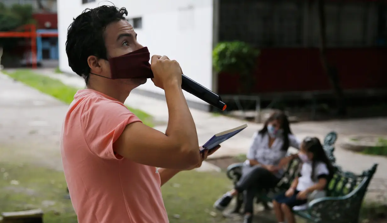 Percibald Garcia menggunakan mikrofon untuk membacakan cerita anak-anak di tengah-tengah kompleks perumahan Tlatelolco di Mexico City pada 18 Juli 2020. Lockdown akibat pandemi corona membuat arsitek muda berusia 27 tahun itu memutuskan untuk berbagi cerita menghibur anak-anak. (AP/Marco Ugarte)