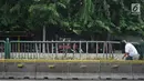 Warga menyeberang melalui pagar pembatas jalur transjakarta yang ditopang bambu di Jalan Otista Raya, Jakarta, Jumat (5/7/2019). Meskipun telah lama rusak, pagar yang berfungsi sebagai pembatas agar orang tidak menyeberang secara sembarangan itu belum juga diperbaiki (Liputan6.com/Immanuel Antonius)