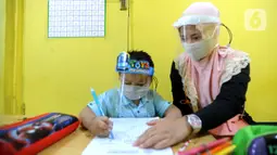 Guru menggunakan face shield saat mengajari murid di Taman Pendidikan Al-Qur'an (TPA) Al-Muthmainnah Cinere, Depok, Rabu (1/7/2020). Jadwal murid diatur dalam beberapa sesion waktu (pagi siang sore) sebagai wajud penerapan sosial distancing dalam kelas. (merdeka.com/Arie Basuki)