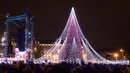 Sejumlah pasangan berdiri di depan pohon Natal raksasa yang menerangi Alun-Alun Katedral di Vilnius, Lithuania, 1 Desember 2017. Pohon Natal megah itu memiliki tinggi sekitar 30 meter yang berhias 70 ribu lampu dan 900 mainan. (AP Photo/Mindaugas Kulbis)