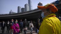 Komuter yang mengenakan masker berjalan melintasi persimpangan di kawasan pusat bisnis di Beijing, Selasa (12/4/2022). AS telah memerintahkan semua staf konsuler non-darurat untuk meninggalkan Shanghai, yang dikunci ketat untuk menahan lonjakan COVID-19. (AP Photo/Mark Schiefelbein)