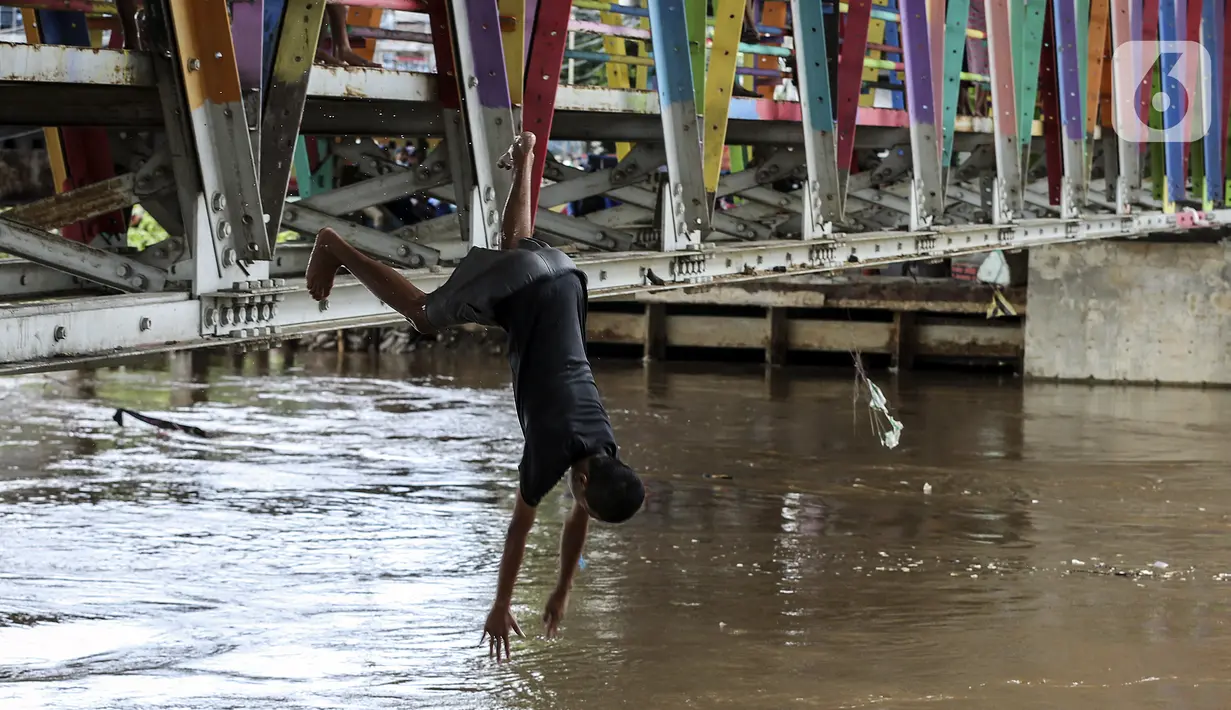 Seorang anak melompat ke Sungai Ciliwung saat banjir melanda Jalan Bina Warga Rt 005/Rw 07 Kelurahan Rawa Jati, Jakarta, Senin (8/2/2021). Banjir setinggi 60-190 cm tersebut disebabkan oleh luapan air Sungai Ciliwung dan curah hujan Jakarta yang tinggi. (Liputan6.com/Johan Tallo)