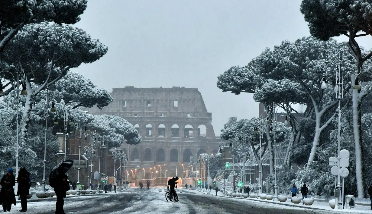 Sejumlah warga berjalan saat salju turun di dekat Colosseum di Roma, Italia (26/2). (AFP Photo/Tiziana Fabi)