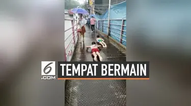 Dua orang bocah Filipina jadikan jembatan penyeberangan orang menjadi tempat bermain perosotan. Mereka memenfaatkan kondisi JPO yang licin karena hujan.