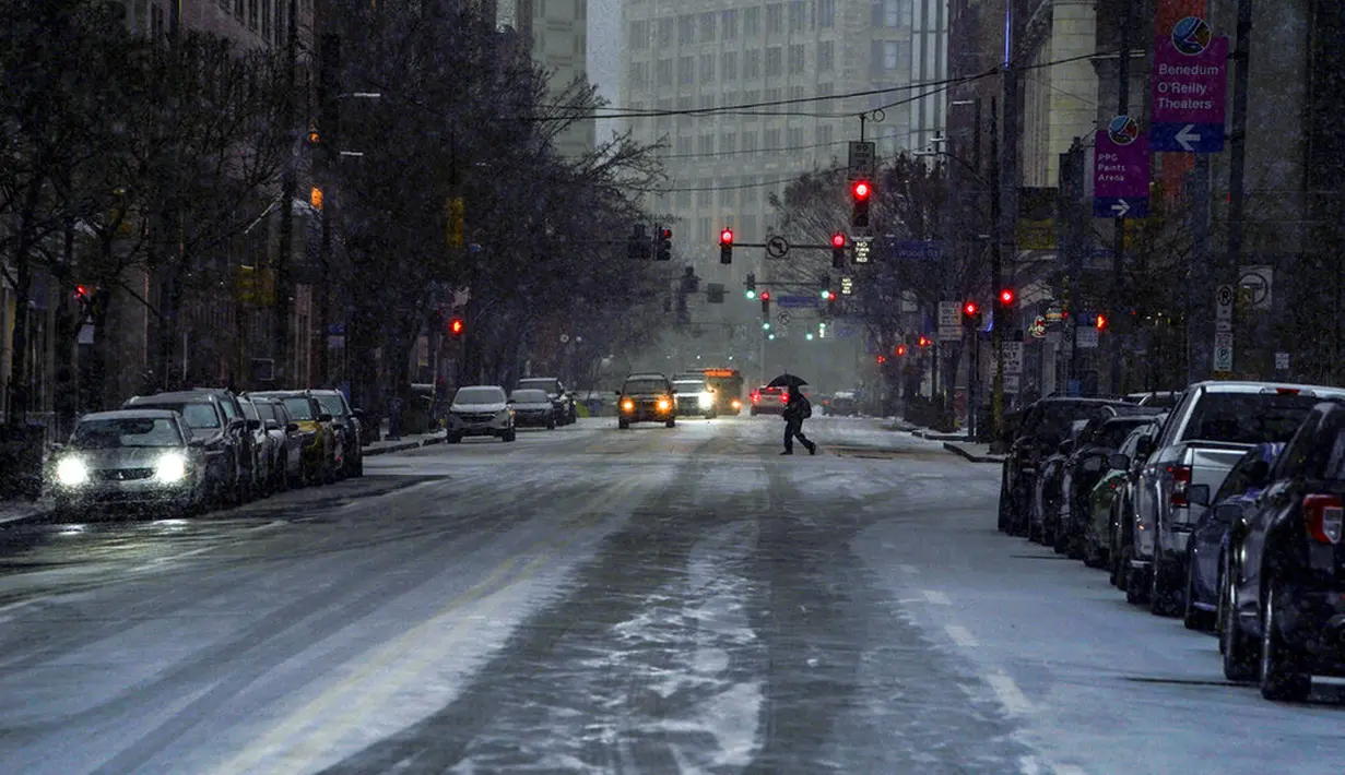 Seorang pejalan kaki menggunakan payung saat melintasi Liberty Avenue saat salju mulai turun selama badai musim dingin yang akan berdampak pada wilayah tersebut di pusat Kota Pittsburgh, Amerika Serikat, 16 Januari 2022. (Alexandra Wimley/Pittsburgh Post-Gazette via AP)
