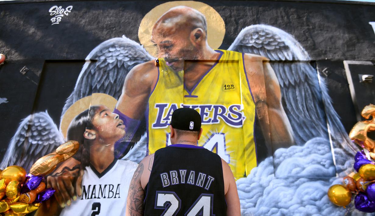 Seorang fans berdiri di depan lukisan mural bintang LA Lakers, Kobe Bryant bersama putrinya, Gianna di Los Angeles, California, Selasa (26/1/2021). Lukisan dibuat untuk mengenang 1 tahun tragedi kecelakaan helikopter yang menewaskan keduanya. (Getty Images via AFP/Harry How)