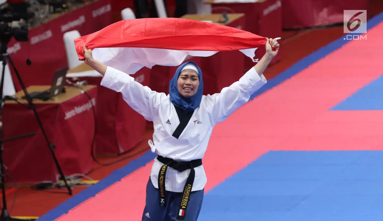 Atlet Taekwondo putri Indonesia, Defia Rosmaniar mengibarkan bendera Merah Putih saat merayakan kemenangan atas Salahshouri Marjan (Iran) pada Final Women Individual Poomsae di JCC, Jakarta, Minggu (19/8). (Liputan6.com/Helmi Fithriansyah)