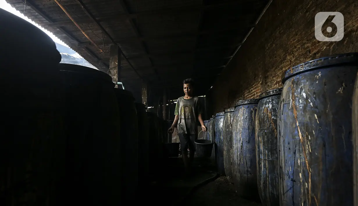 Pekerja berjalan melewati deretan wadah saat membuat alkohol tradisional di industri rumahan Desa Bekonang, Kecamatan Mojolaban, Kabupaten Sukoharjo, Jawa Tengah, Rabu (18/11/2020). Minuman tersebut disaring menggunakan karung beras agar tidak ada kotoran yang tersisa. (Liputan6.com/Johan Tallo)