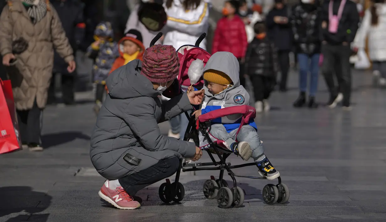 <p>Seorang wanita memberi makan makanan ringan untuk seorang anak di kereta dorong di jalan perbelanjaan pejalan kaki Qianmen, tempat wisata populer di Beijing, Selasa (17/1/2023). Biro Statistik Nasional di China mencatat, populasi China telah menurun sekitar 850 ribu, menjadi 1,4 miliar terhitung hingga akhir 2022. (AP Photo/Andy Wong)</p>