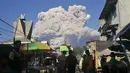 Orang-orang menyaksikan Gunung Sinabung memuntahkan material vulkanik saat meletus di Karo, Sumatera Utara, Selasa (2/3/2021).  Erupsi Gunung Sinabung juga mengendapkan abu di desa-desa terdekat. (AP Photo/Sugeng Nuryono)