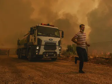 Seorang pria berlari di Desa Sirtkoy yang dilanda kebakaran, dekat Manavgat, Antalya, Turki, Minggu (1/8/2021). Menurut para pejabat, lebih dari 100 kebakaran hutan telah dikendalikan di Turki. (AP Photo)