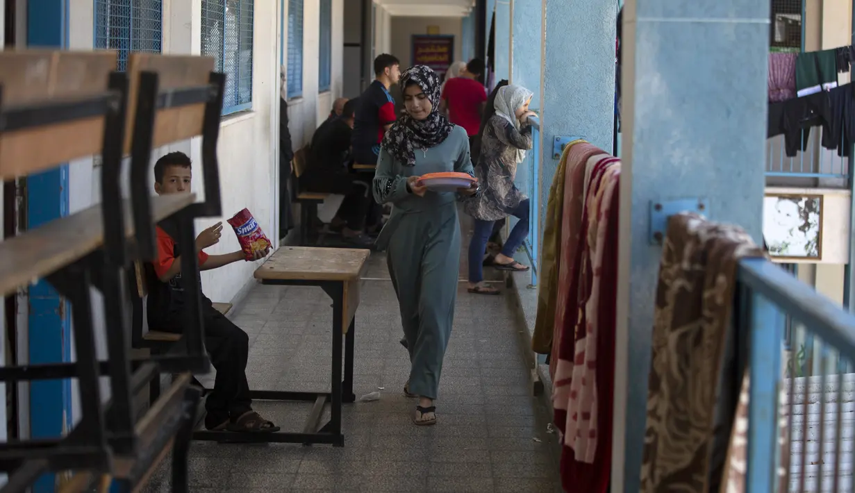 <p>Seorang wanita berjalan saat berlindung di sekolah yang dikelola oleh PBB setelah melarikan diri dari serangan rudal hebat Israel di pinggiran Kota Gaza, Rabu (19/5/2021). Mereka terpaksa meninggalkan rumah di tengah semakin gencarnya serangan udara dari militer Israel. (AP Photo/Khalil Hamra)</p>