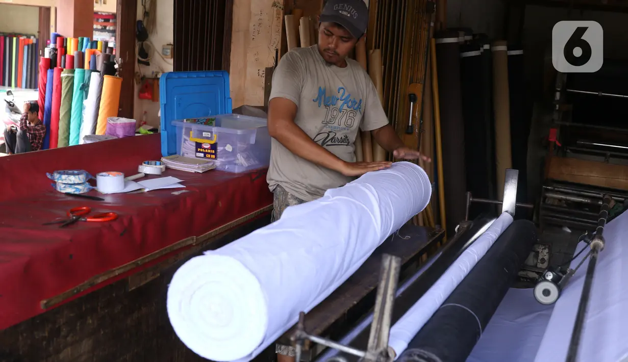 Pedagang menggulung bahan kain yang akan dijual di kawasan Tangerang, Banten, Sabtu (25/9/2021). Program Restrukturisasi Mesin/Peralatan tahun 2021 bertujuan meningkatkan kembali performa industri Tekstil dan Produk Tekstil (TPT) sebagai sektor strategis. (Liputan6.com/Angga Yuniar)