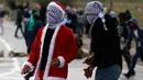 Seorang demonstran Palestina mengenakan kostum Santa Claus bersiap melempar batu ke arah pasukan keamanan Israel saat terjadi bentrokan di pos pemeriksaan Atarot di pinggiran utara Yerusalem (19/12). (AFP Photo/Abbas Momani)