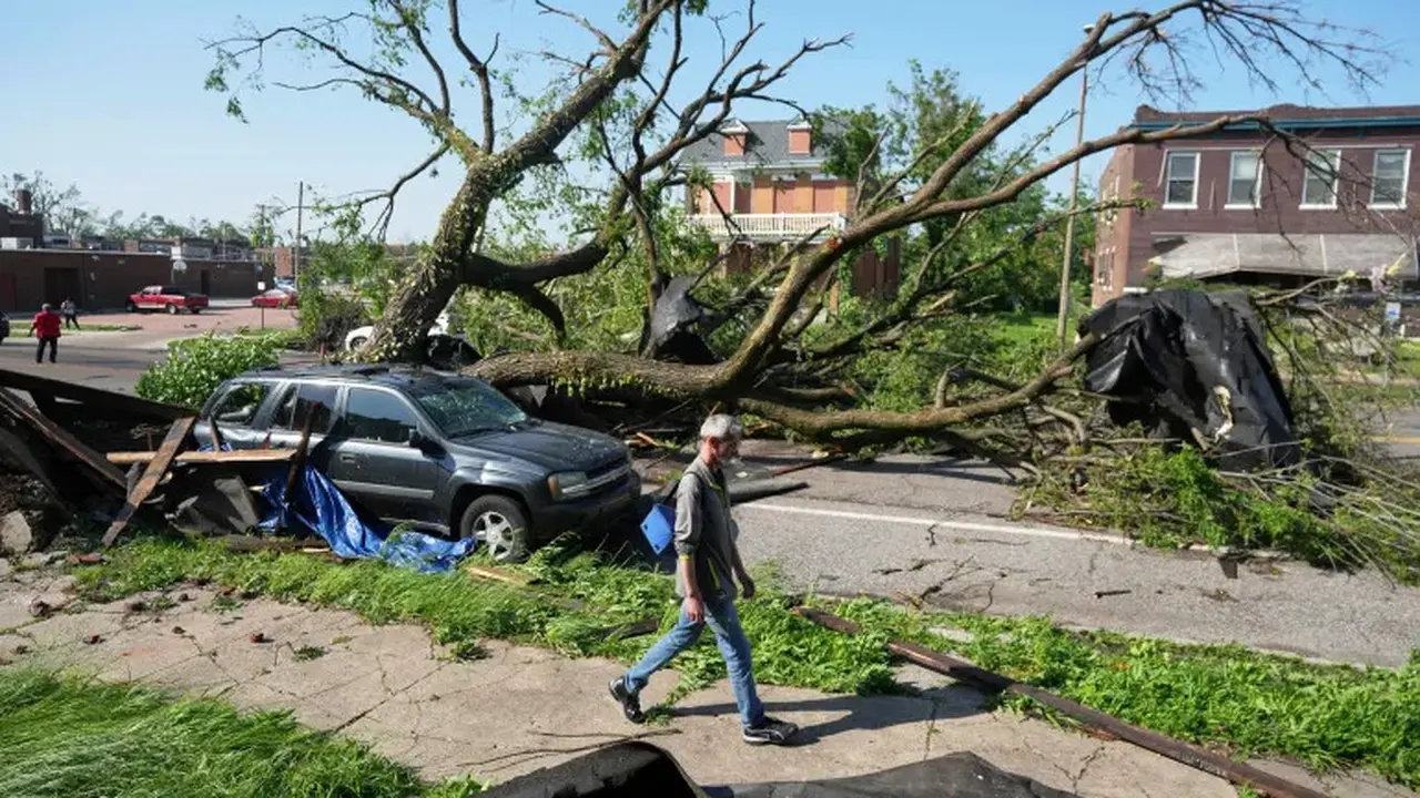 Seorang pria berjalan melewati pohon besar yang menghalangi jalan setelah badai dahsyat melanda St. Louis, Missouri, AS [Jeff Roberson/AP]
