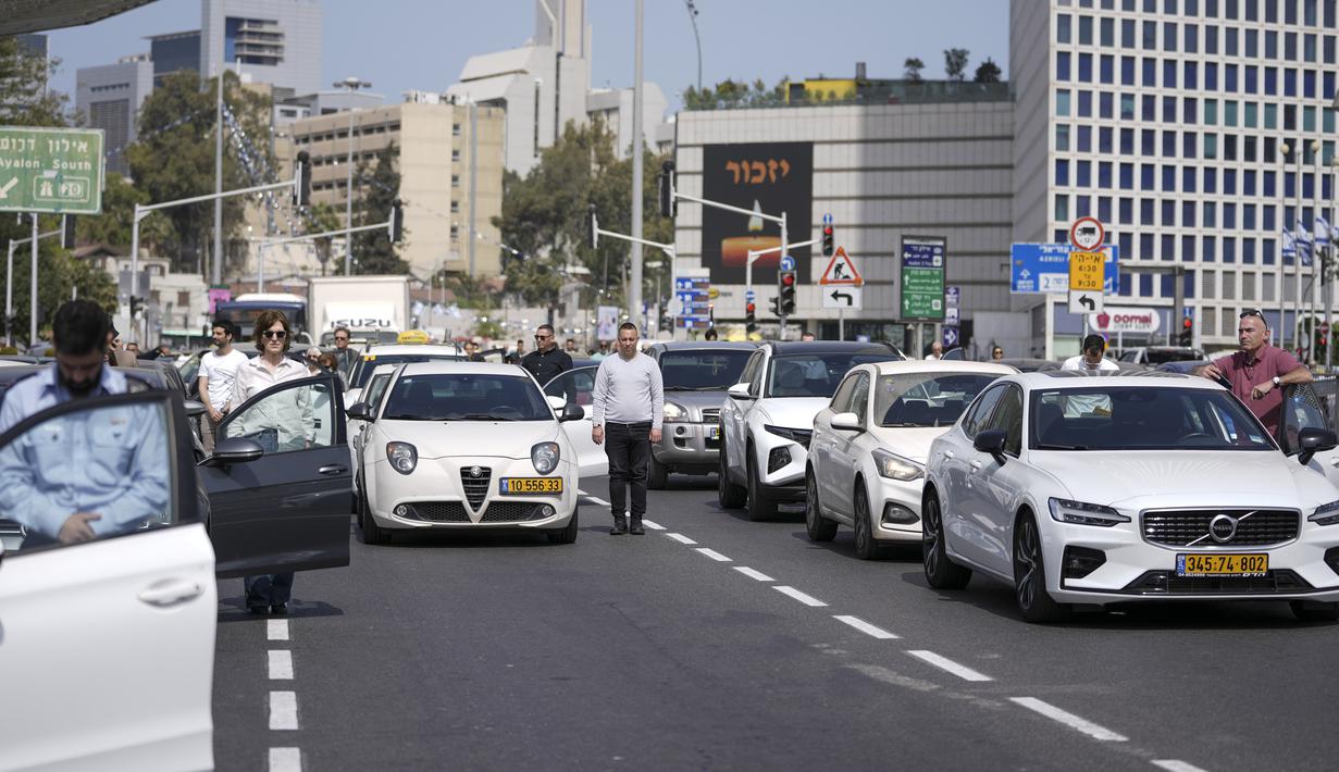 <p>Warga Israel berdiri diam di samping mobil mereka di jalan utama saat sirene dua menit berbunyi untuk mengenang para korban Holocaust di Tel Aviv, Israel, 28 April 2022. Selama Hari Peringatan Holocaust restoran dan tempat hiburan ditutup, sementara program radio dan TV berfokus pada film dokumenter Holocaust serta wawancara dengan para penyintas. (AP Photo/Ariel Schalit)</p>