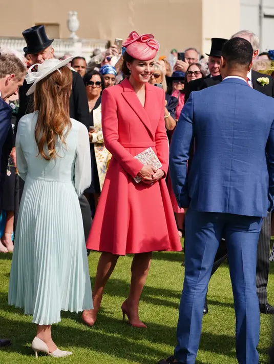 Kate Middleton, Duchess of Cambridge dari Inggris berbicara kepada para tamu di Pesta Taman Kerajaan di Istana Buckingham di London (18/5/2022). Kate Middleton mengenakan gaun mantel koral dengan topi dengan warna yang sama. (AFP/Pool/Dominic Lipinski)