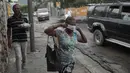 <p>Seorang wanita berjalan melewati pihak berwenang setempat yang memindahkan jenazah pria yang dibakar massa di Port-au-Prince, Haiti, Selasa (25/4/2023). (AP Photo/Odelyn Joseph)</p>