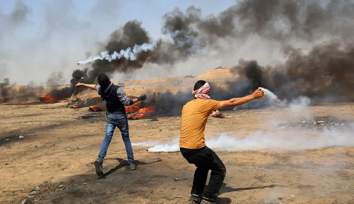 Dua pemuda Palestina berusaha menghalau dan melempar balik gas air mata yang ditembakkan oleh paskuan Israel di jalur Gaza (11/5). (AFP Photo/Mohammed Abed)