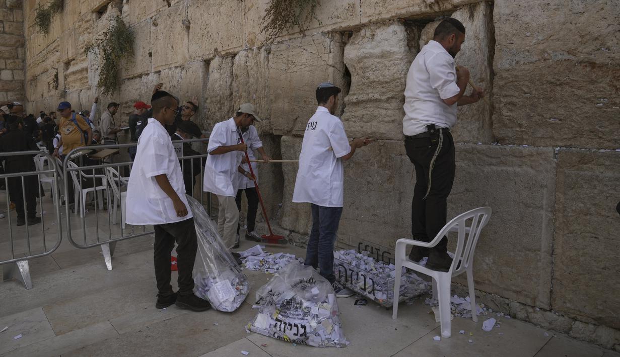 Para pekerja memindahkan catatan doa yang ditinggalkan pengunjung dari celah di antara batu-batu di Tembok Barat, situs paling suci tempat orang Yahudi dapat berdoa di Kota Tua Yerusalem, Selasa, 20 September 2022, menjelang Rosh Hashana, Tahun Baru Yahudi. Catatan dimakamkan di pemakaman terdekat menurut tradisi Yahudi. Operasi dilakukan dua kali setahun sebelum Rosh Hashana dan sebelum liburan Paskah di musim semi. (AP/Mahmoud Illean)
