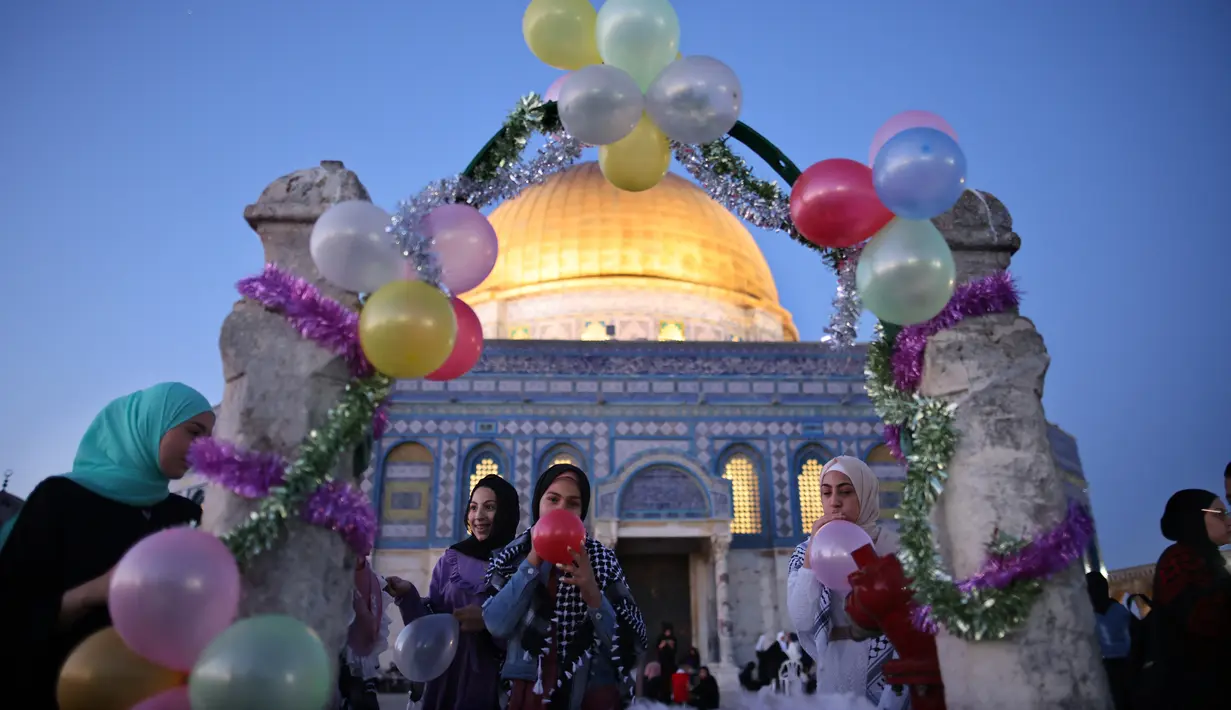 Wanita Muslim meniup balon saat jamaah merayakan hari raya Idul Fitri, yang menandai akhir bulan suci Ramadhan, setelah sholat subuh di kompleks masjid Al-Aqsa, dengan latar belakang masjid Kubah Bat  di Yerusalem Tua (13/5/2021). (AFP/Ahmad Gharabli)