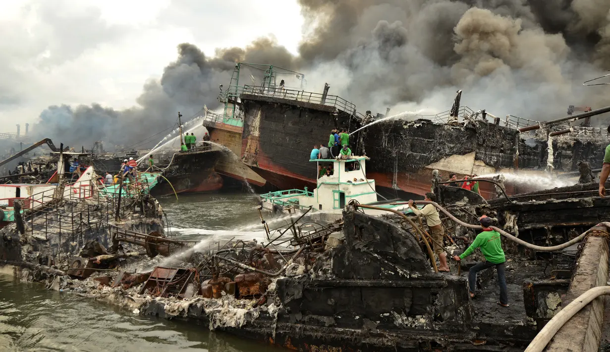 Pekerja dan petugas pemadam kebakaran mencoba memadamkan api di kapal nelayan di Pelabuhan Benoa, Denpasar, Bali, Senin (9/7). Kebakaran besar melalap 39 kapal yang tengah bersandar di dermaga. (SONNY TUMBELAKA/AFP)