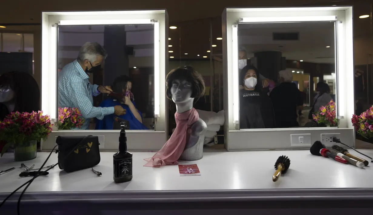 Refleksi seorang perempuan di cermin saat memotong rambut dalam acara Bulan Peduli Kanker Payudara di sebuah mal di Caracas, Venezuela, Sabtu (16/10/2021). Rambut yang dipotong akan disumbangkan untuk membuat wig bagi pasien kanker. (AP Photo/Ariana Cubillos)
