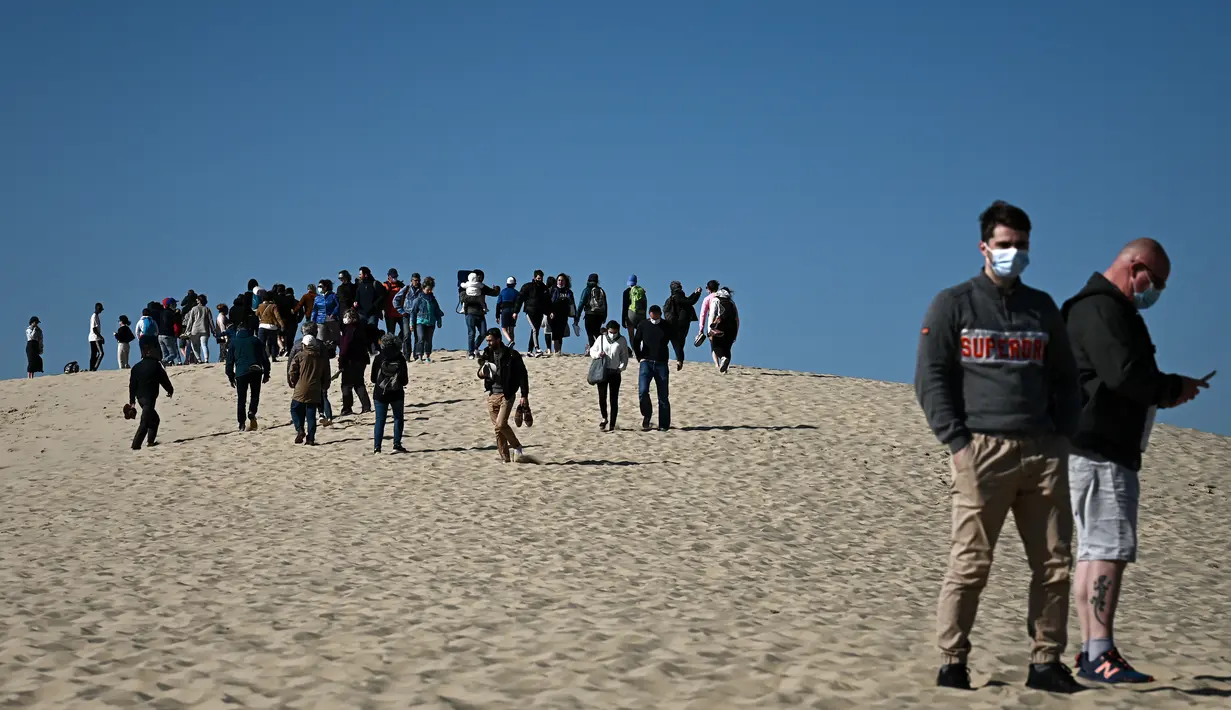 Orang-orang menikmati hari yang cerah di "Dune du Pilat" di La Teste-de-Buch, dekat Teluk Arcachon di barat daya Prancis pada 3 April 2021. The Dune of Pilat merupakan gurun pasir tertinggi di Eropa, yaitu sekitar 110 meter di atas permukaan air laut. (Philippe LOPEZ / AFP)