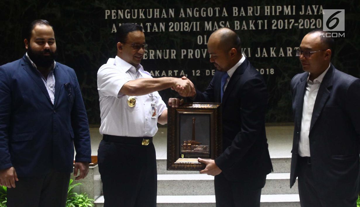 Gubernur DKI Jakarta Anies Baswedan (dua kiri) menyerahkan cendera mata kepada Ketua Umum HIIPMI Jaya Afifuddin Suhaeli Kalla saat pelantikan anggota HIPMI Jaya di Balai Kota Jakarta, Rabu (12/12). (Liputan6.com/Angga Yuniar)