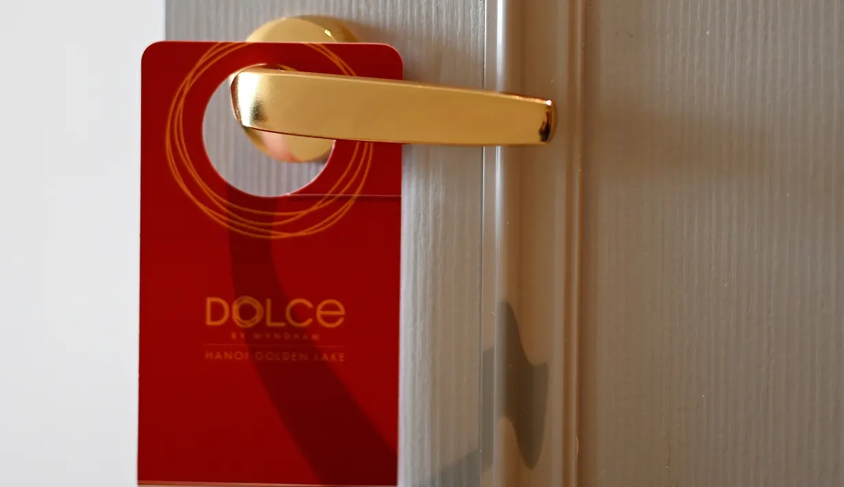 Sebuah plakat tergantung pada gagang pintu kamar hotel Dolce Hanoi Golden Lake yang baru saja diresmikan di Hanoi, Vietnam pada Kamis (2/7/2020). Hotel tersebut merupakan hotel berlapiskan emas 24 karat pertama di dunia. (Manan VATSYAYANA / AFP)