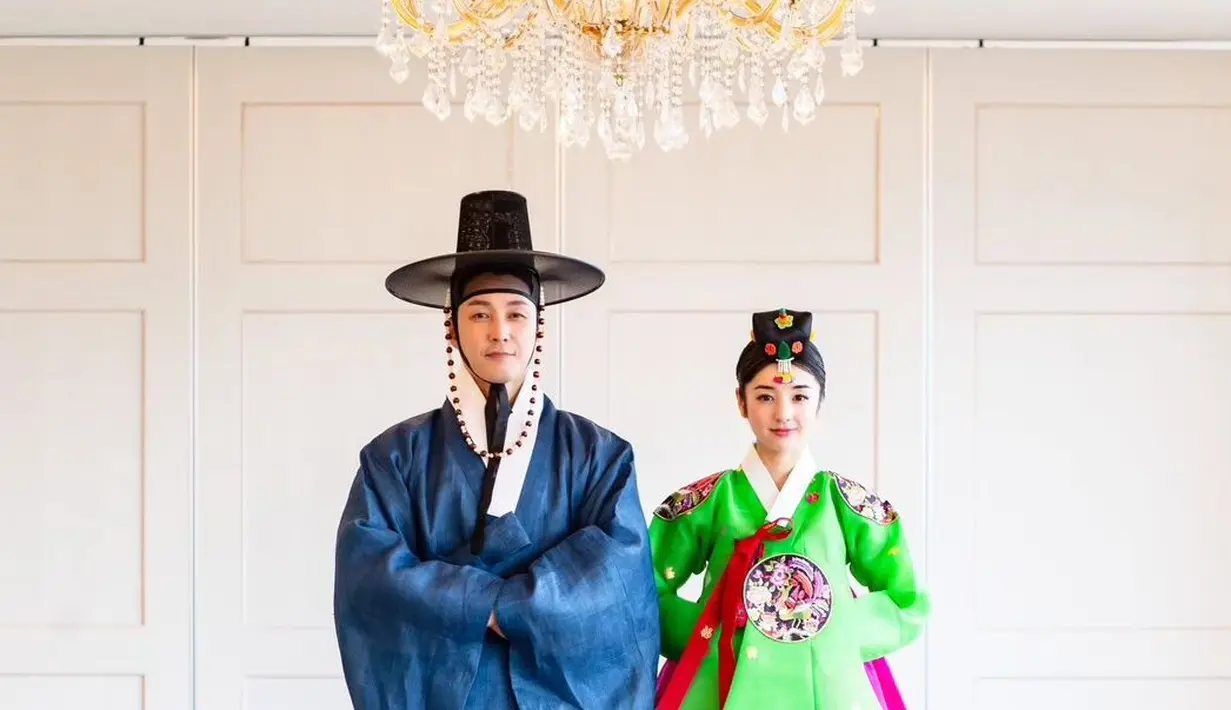 Di foto yang lain, Shim Hyung Tak dan Hirai Saya mengenakan baju adat Korea, yaitu hanbok. Hanbok yang dikenakan Shim Hyung Tak berwarna biru jeans, lengkap dengan topi hitamnya bak pangeran di zaman Joseon, sedangkan Hirai Saya mengenakan hanbok berwarna cerah, yaitu hijau dan merah keunguan, riasan wajah bold, dan gaya rambut, serta aksesori bak pengantin zaman dulu. [Foto: Instagram/tak9988]