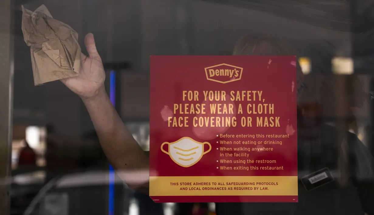 Seorang pekerja membersihkan pintu restoran Denny di Garden Grove, California, Senin (17/5/2021). California tidak akan mencabut aturan maskernya hingga 15 Juni untuk memberikan waktu persiapan kepada publik dan bisnis serta memastikan kasus COVID-19 tetap rendah. (AP Photo/Jae C. Hong)
