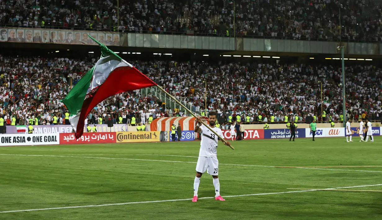 Pemain timnas Iran, Ramin Rezaeian mengibarkan bendera nasional usai mengalahkan Uzbekistan pada kualifikasi Grup A zona Asia, Senin (12/6). Iran menjadi negara ketiga yang memastikan diri tampil ke putaran final Piala Dunia 2018. (AP Photo/Vahid Salemi)