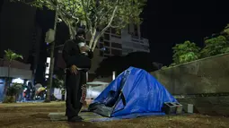 Marcio, gelandangan yang tinggal di jalanan, menjaga dirinya tetap hangat di malam yang dingin di Sao Paulo, Brasil, Kamis (29/7/2021). Setidaknya 43 kota di Brasil mengalami hujan salju atau freezing rain yang membuat benda-benda sekitarnya diselimuti es pada Rabu malam. (AP Photo/Marcelo Chello)