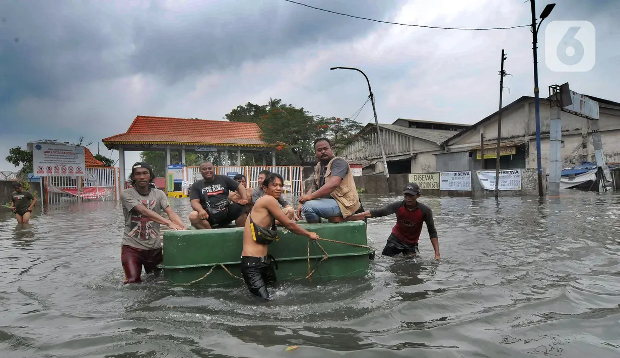 Warga menaiki benda terapung untuk melewati banjir rob di kawasan Pelabuhan Sunda Kelapa, Jakarta, Selasa (7/12/2021). Banjir rob setinggi satu meter memutus Jalan Kerapu yang menghubungkan Ancol-Pluit. (merdeka.com/Arie Basuki)