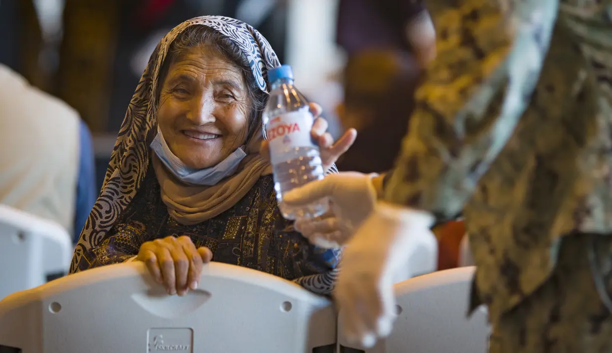 Seorang wanita Afghanistan tersenyum setelah diberi sebotol air usai turun dari pesawat angkatan udara AS di Naval Station di Rota, Spanyol, Selasa (31/8/2021).  Amerika Serikat menyelesaikan penarikannya dari Afghanistan Senin malam, mengakhiri perang terpanjang Amerika. (AP Photo/Marcos Moreno)
