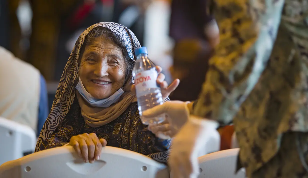 Seorang wanita Afghanistan tersenyum setelah diberi sebotol air usai turun dari pesawat angkatan udara AS di Naval Station di Rota, Spanyol, Selasa (31/8/2021).  Amerika Serikat menyelesaikan penarikannya dari Afghanistan Senin malam, mengakhiri perang terpanjang Amerika. (AP Photo/Marcos Moreno)