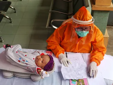 Bidan mengenakan alat pelindung diri (APD) saat melakukan imunisasi kepada bayi di Puskesmas Karawaci Baru, Tangerang, Banten, Rabu (13/5/2020). Pelayanan imunisai sesuai jadwal ini diberikan kepada bayi untuk menambah kekebalan imun tubuh. (Liputan6.com/Angga Yuniar)