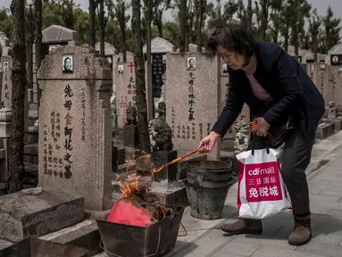 Seorang wanita membakar dupa sebagai persembahan selama festival Qingming di sebuah pemakaman di Shanghai (6/6). Qingming adalah ritual tahunan etnis Tionghoa untuk bersembahyang dan ziarah kubur sesuai dengan ajaran Khong Hu Cu. (AFP/Johannes Eisele)