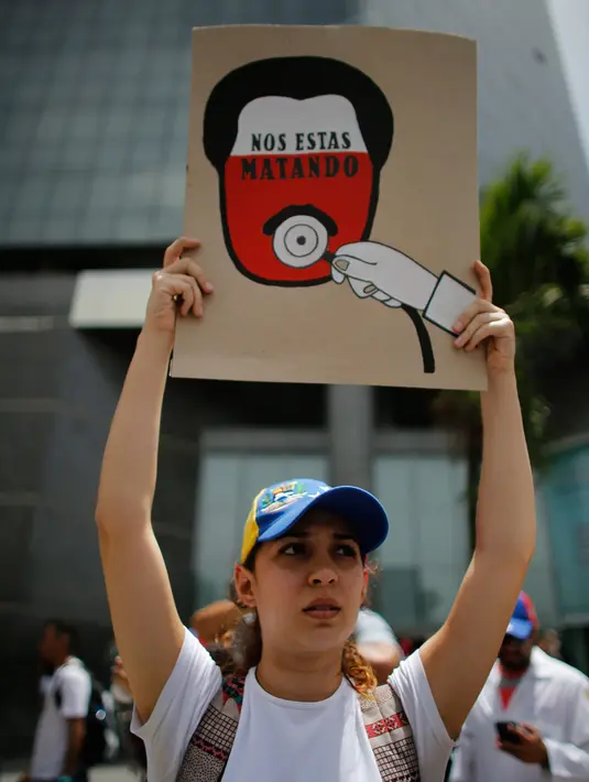 Seorang dokter muda membawa poster bertuliskan "You are killing us," saat unjuk rasa menuntut Presiden Venezuela Nicolas Maduro di Caracas, Venezuela, (22/5). Sedikitnya 46 orang telah meninggal dunia. (AP Photo/Ariana Cubillos)