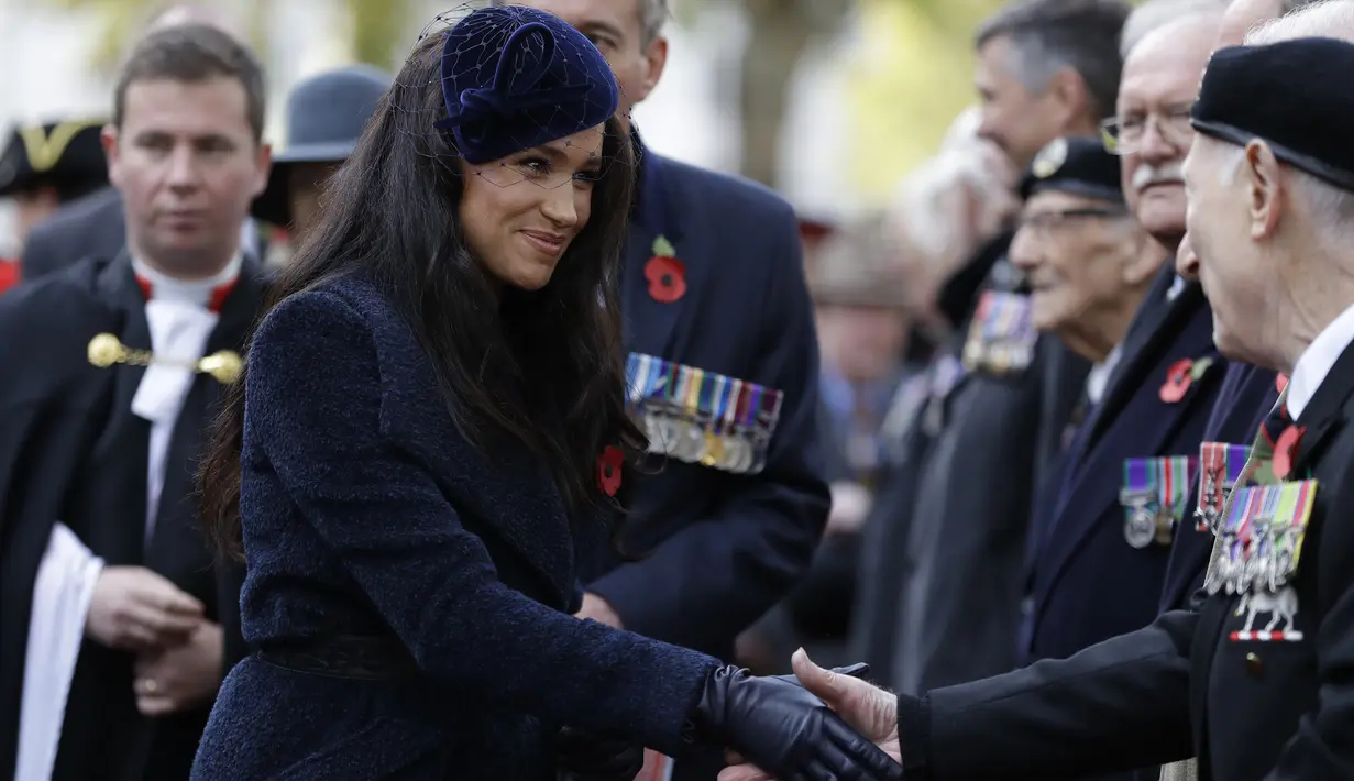 Duchess of Sussex Meghan Markle bersalaman dengan veteran perang saat menghadiri Field of Remembrance, London (7/11/2019). Meghan Markle tampil cantik mengenakan mantel Boucle Alpaca biru tua dari koleksi Sentaler dan topi beludru kerudung jala koleksi Philip Treacy. (AFP Photo/Kirsty Wigglesworth)