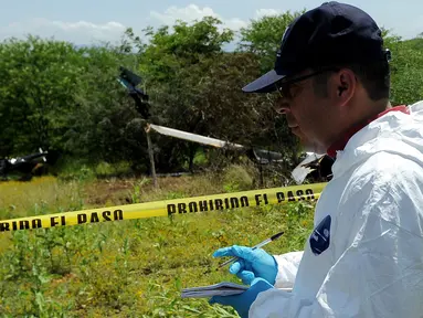 Petugas forensik berdiri di dekat puing helikopter polisi yang diduga jatuh ditembak oleh sekelompok geng kartel narkoba di Michoacan, Meksiko barat, Rabu (7/9). Insiden ini menyebabkan empat orang di helikopter tersebut tewas. (PEDRO PARDO/AFP)