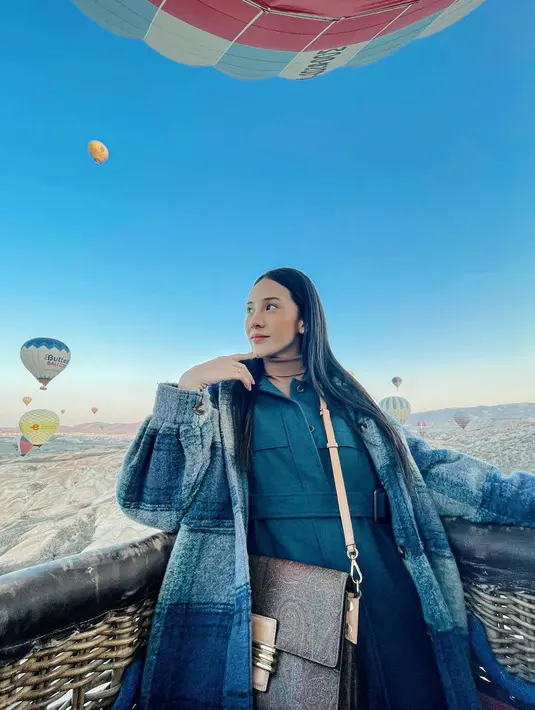 Di atas balon udara, Anya juga berpose memperlihatkan OOTDnya. Ia tampak mengenakan turtleneck cokelat, dilapisinya dengan structured jacket panjang, dilengkapi belt di bagian pinggang dan kantung di dada kanan-kiri. Anya masih tampak melapisinya lagi dengan jaket super besar bermotif kotak-kotak sebagai outerwear. Ia juga terlihat membawa sling bag berbentuk kotak yang besar, menata rambutnya dengan gaya sederhana mengenakan bandana hitam polos. Foto: Instagram.