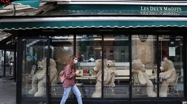 Pejalan kaki melintas di depan boneka beruang raksasa di kafe Les Deux Magots yang ditutup di Paris, Prancis, pada 16 Desember 2020. Boneka beruang itu dipajang untuk menggantikan pengunjung saat restoran tutup selama penerapan jam malam guna menekan laju penyebaran COVID-19. (Xinhua/Gao Jing)