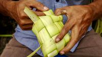 Seorang penjual menganyam daun kelapa atau kulit ketupat sambil menunggu pelanggan di sebuah pasar tradisional di Jakarta pada 2 April 2024. (BAY ISMOYO/AFP)
